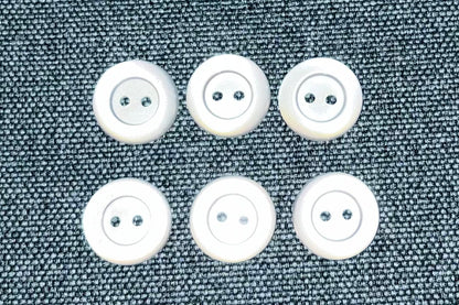 Six white buttons on a textured gray fabric background
