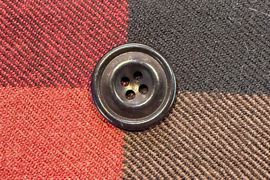 Close-up of a button on checkered fabric with red, beige, and gray colors.
