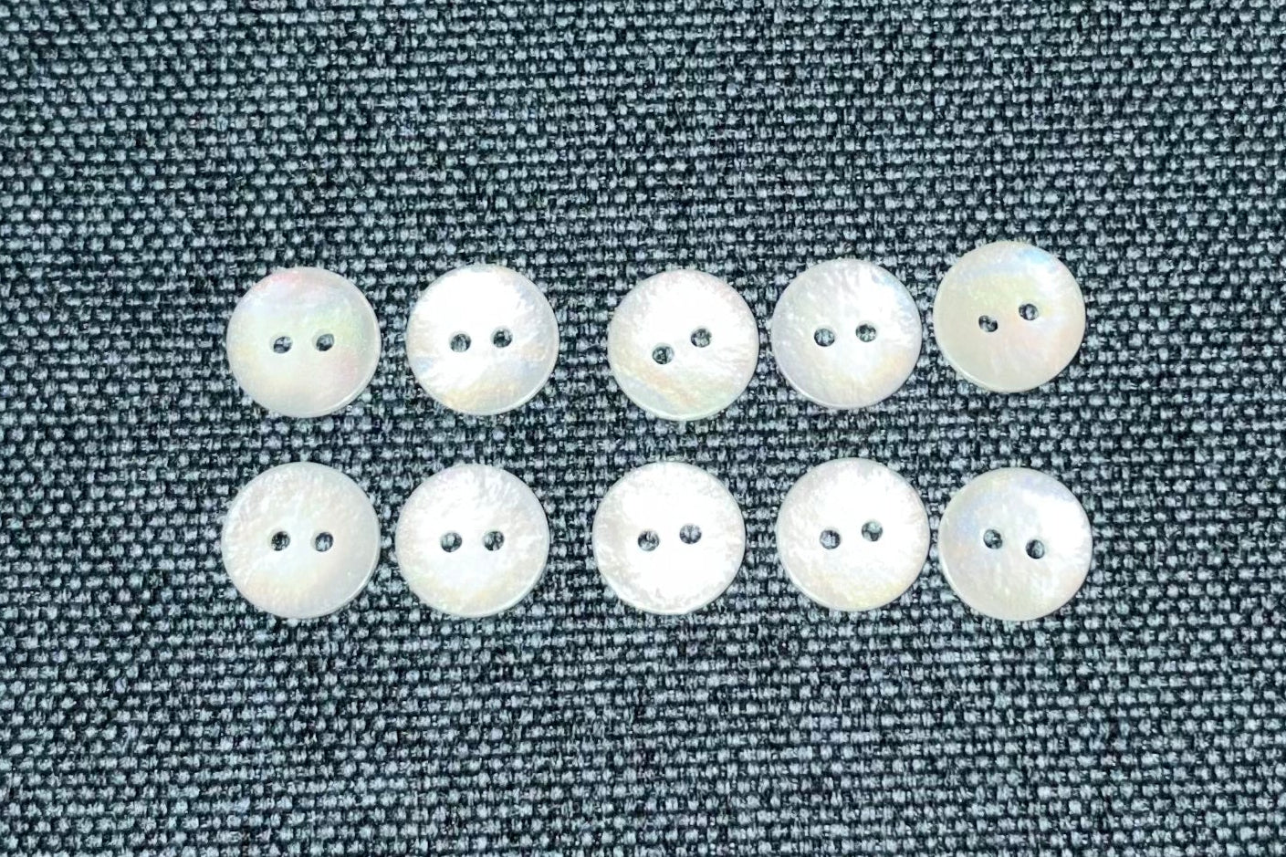 Ten white buttons on a textured fabric surface.
