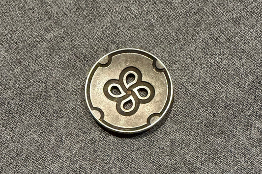 Metallic button with a four-leaf clover design on a gray fabric background
