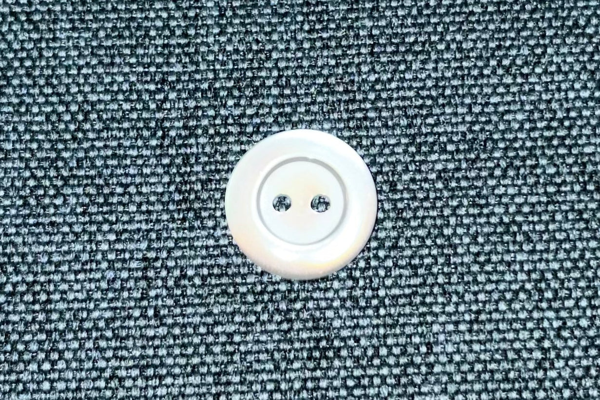Close-up of a white button on a textured blue fabric.