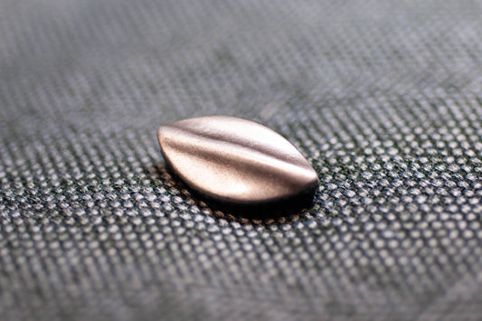 Metallic teardrop-shaped button on a textured gray surface